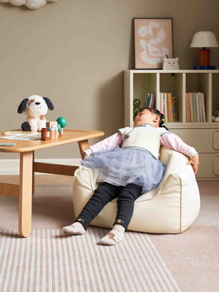 Child sitting on a bean bag chair in a room with a table and books.