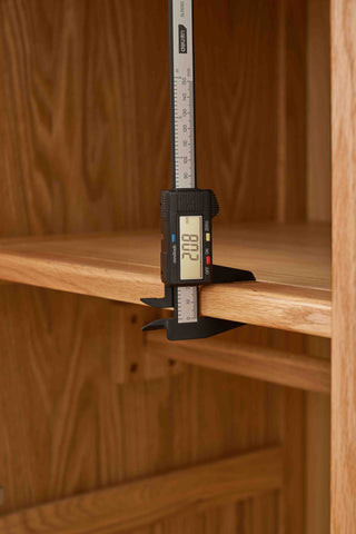 Digital caliper measuring a wooden shelf against a wooden background