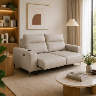 A modern beige leather extendable sofa in a beautifully styled, warm-toned living room with a wooden bookshelf, pleated floor lamp, and round coffee table.