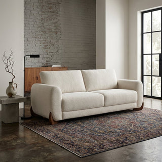 An off-white boucle 3 seater sofa with dark wood legs, styled in a modern living room setting on a patterned area rug.