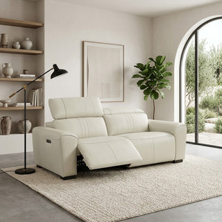 An off-white leather reclining loveseat sofa in a modern, minimalist living room setting with a black floor lamp, wooden shelves, and a large arched window.