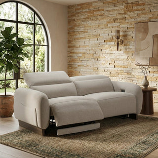 Beige fabric power recliner sofa in a living room with stone wall and large window