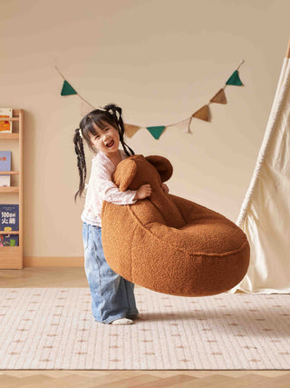 Child holding a large brown teddy bear in a room with a bookshelf and decorative flags.