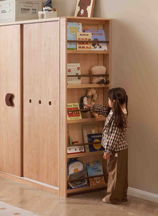 Child interacting with a wooden bookshelf filled with books and toys in a room.