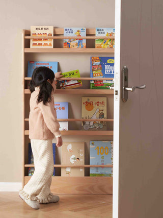 Child looking at books on a wooden bookshelf in a room with a door.