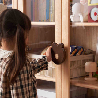 Child opening a wooden cabinet with a bear-shaped handle.