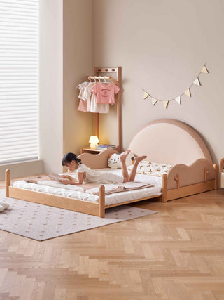 Child playing on a wooden bed in a room with a clothes rack and decorative lights.