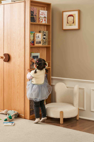 Child playing with a wooden bookshelf in a room with a chair and toys.