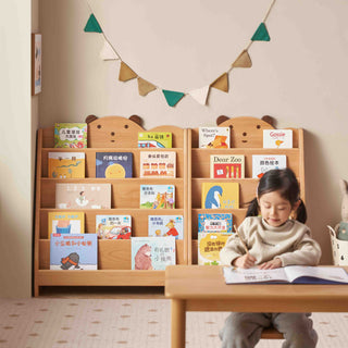Child sitting at a desk reading a book in front of a wooden bookshelf with books.