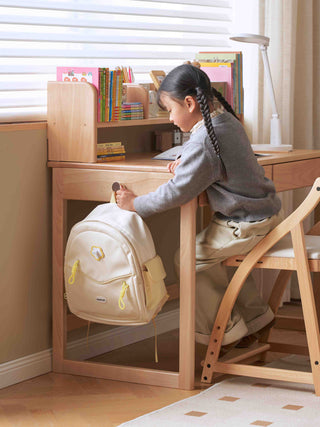 Child sitting at a kids study table with a backpack, surrounded by books and stationery.