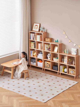 Child sitting at a small wooden table in front of a nursery bookshelf filled with books and decorative items.
