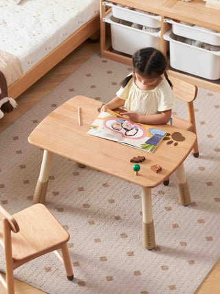 Child sitting at a small wooden table with a book and toys on a patterned rug.