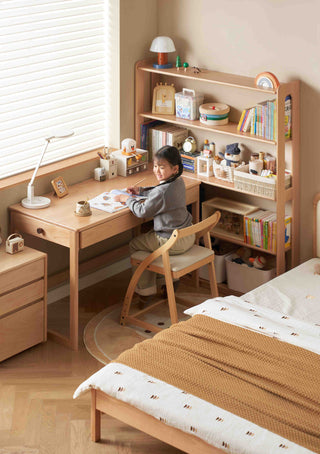 Child sitting at a wooden desk in a room with a bookshelf and bed.