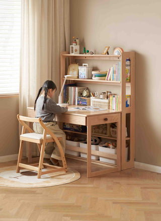 Child sitting at a wooden desk with shelves in a room with light-colored walls and floor.