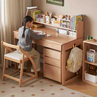 Child sitting at a wooden kids desk in a room with books and toys.