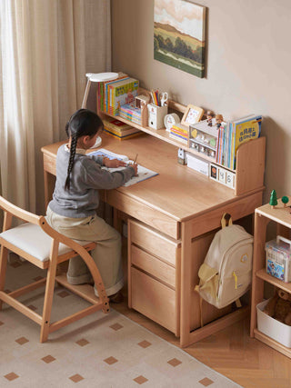Child sitting at a wooden kids study table in a room with books and a backpack.