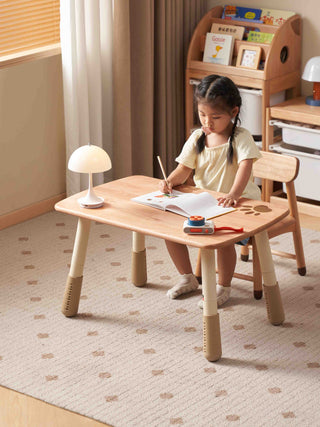 Child sitting at a wooden play table with a lamp in a room with shelves and books.