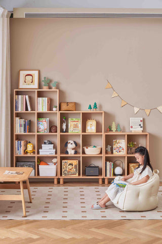 Child sitting in a chair in front of a nursery bookshelf in a room with a beige wall.