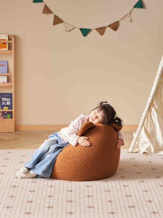 Child sitting on a brown bean bag chair in a cozy room with a bookshelf and decorative flags.