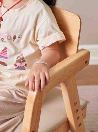Child sitting on a wooden chair wearing a white shirt with cartoon designs.