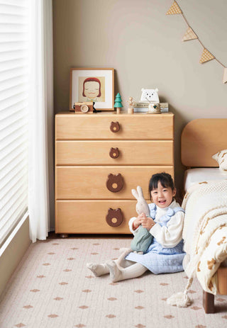 Child sitting on the floor next to a wooden kids dresser in a child's room
