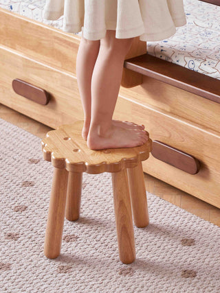 Child standing on a wooden step stool in a bedroom.