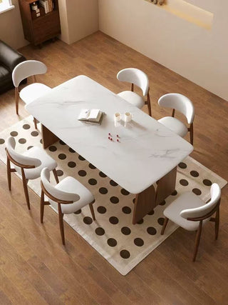 Dining room with a marble table and white chairs on a patterned rug.