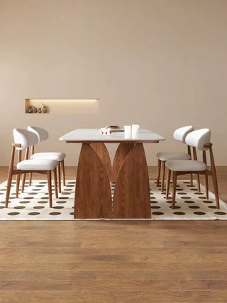 Dining room with a wooden table and white chairs on a patterned rug.