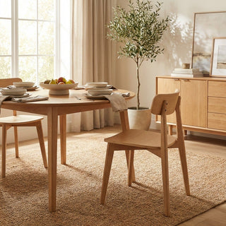 Dining room with wooden table and chairs, fruit bowl, and plant.