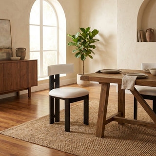 Dining room with wooden table, chairs, and a plant in a well-lit room.