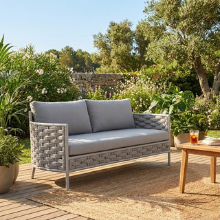 Gray outdoor sofa with cushions on a wooden deck surrounded by greenery