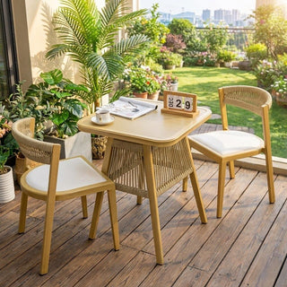 Outdoor dining set with table and chairs on a wooden deck, surrounded by plants and a garden view.
