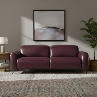 Maroon leather sofa in a living room with a painting and plant on a neutral wall.