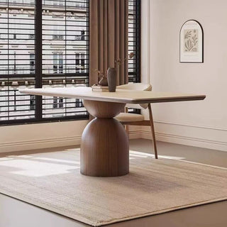 Modern dining table with wooden base and marble top in a room with large windows.