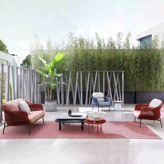 Modern outdoor furniture set with red chairs and a coffee table on a pink rug, surrounded by greenery.