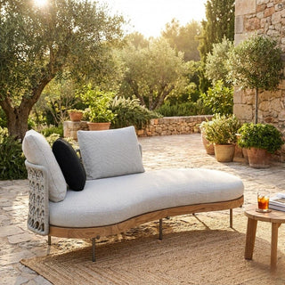 Outdoor lounge chair with cushions on a stone patio surrounded by greenery