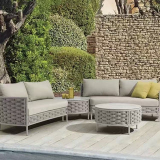 Outdoor patio furniture set with cushions on a wooden deck against a stone wall and greenery.