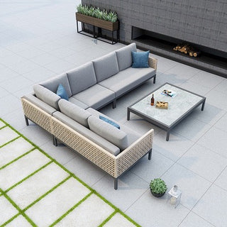 Outdoor patio furniture set with gray sectional sofa, wicker chairs, and coffee table on a tiled patio.