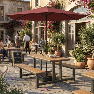 Outdoor patio setting with a large red umbrella parasol, tables, and benches in a stone-paved area.