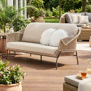Outdoor patio setting with wicker sofa, cushions, and plants on a wooden deck.