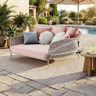 Outdoor patio with a pink cushioned sofa, umbrella, and small table by a pool.