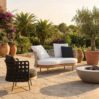 Outdoor patio with a sofa, chair, and fire pit surrounded by plants and flowers.