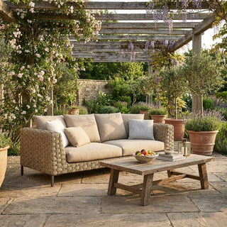 Outdoor patio with wicker sofa, wooden coffee table, and potted plants under a wooden pergola.