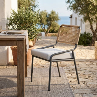 Outdoor setting with a wooden table and wicker chair on a stone patio.