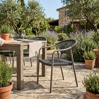 Outdoor setting with wooden table and chairs surrounded by potted plants and a stone building.
