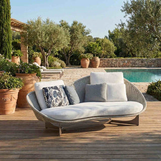 Outdoor sofa with cushions on a wooden deck by a pool with greenery.