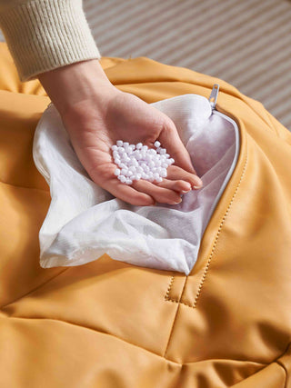 Person holding a small bag of white beads against a yellow jacket.