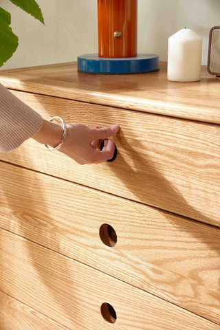Person opening a wooden drawer with a hand, surrounded by candles and decorative items.