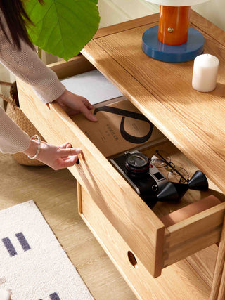 Person opening a wooden drawer with items inside, surrounded by a cozy indoor setting.