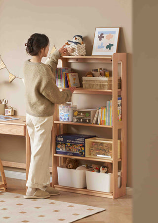Person organizing a wooden bookshelf filled with books and toys in a room.
